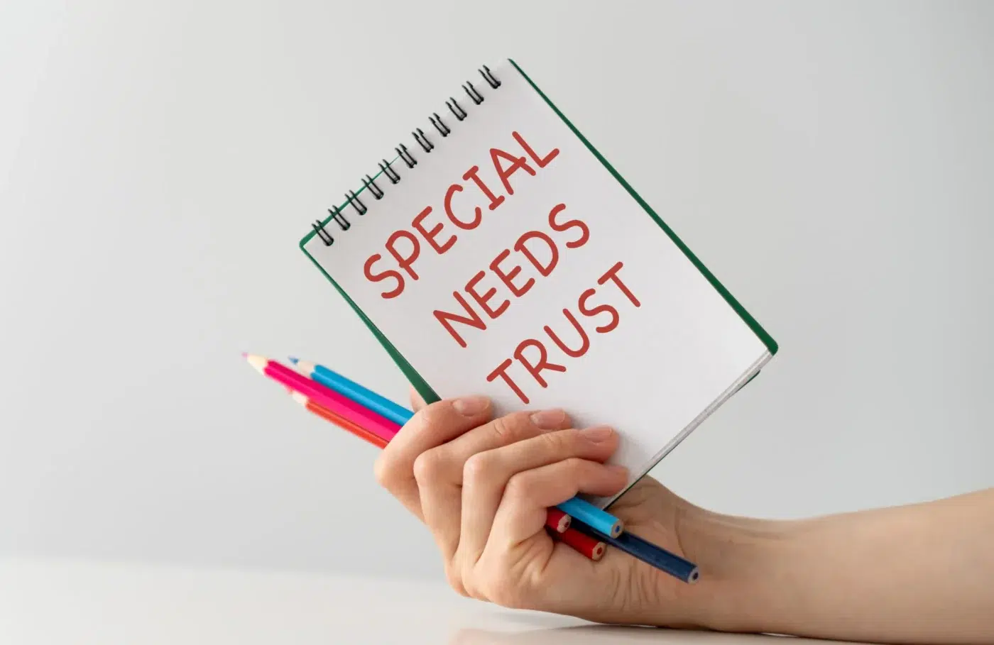 A hand holding a notebook labeled Special Needs Trust along with several colored pencils.
