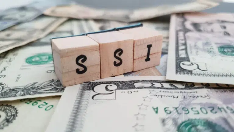Wooden blocks spelling “SSI” placed on top of scattered U.S. dollar bills, representing disability-related financial eligibility.