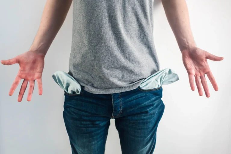 Person wearing jeans and a gray shirt with empty pockets turned inside out, symbolizing financial loss or lack of funds.