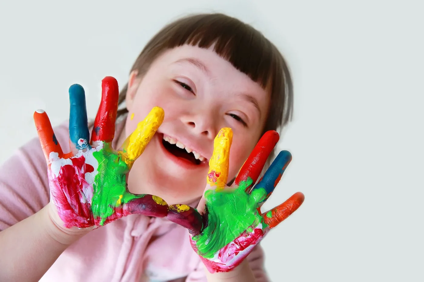 A smiling child with painted hands held up toward the camera, showing bright multicolored paint on both palms.