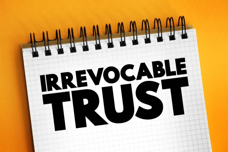Notebook with the words “Irrevocable Trust” written in bold black letters on a grid page against a bright orange background.