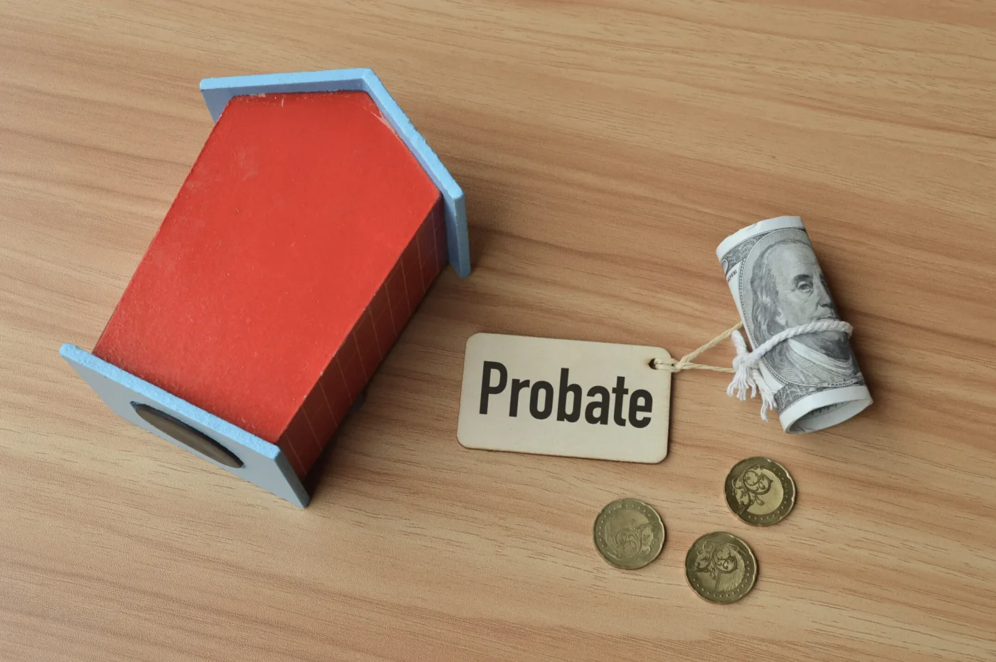 Wooden house model, rolled-up cash, and coins beside a probate tag on a wooden table