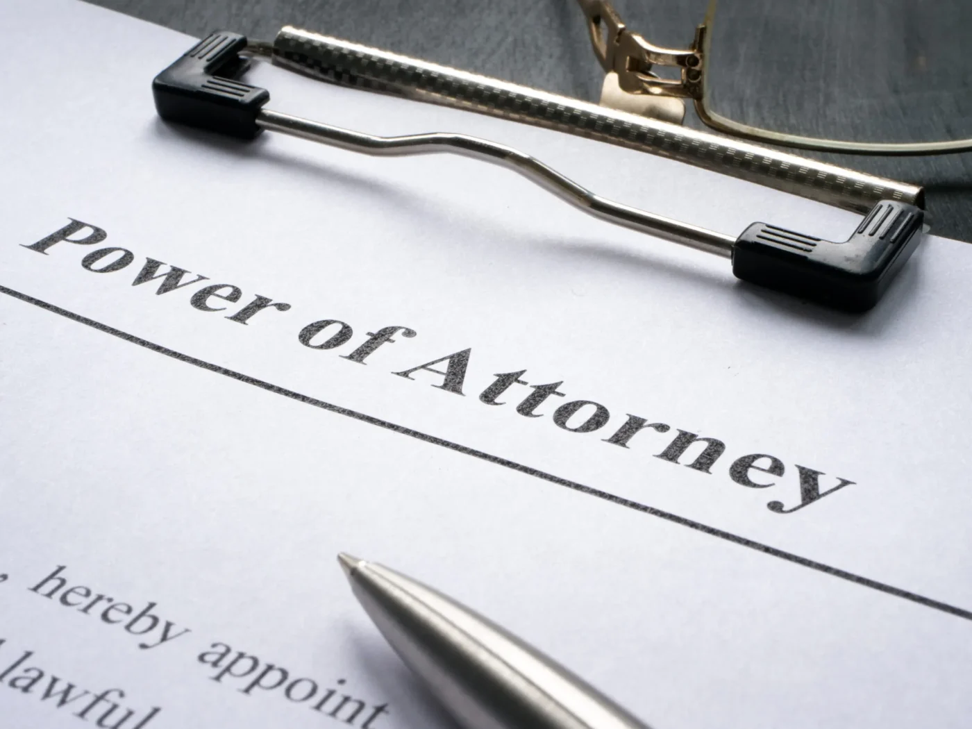lose-up of a Power of Attorney document on a clipboard with a pen and reading glasses nearby.