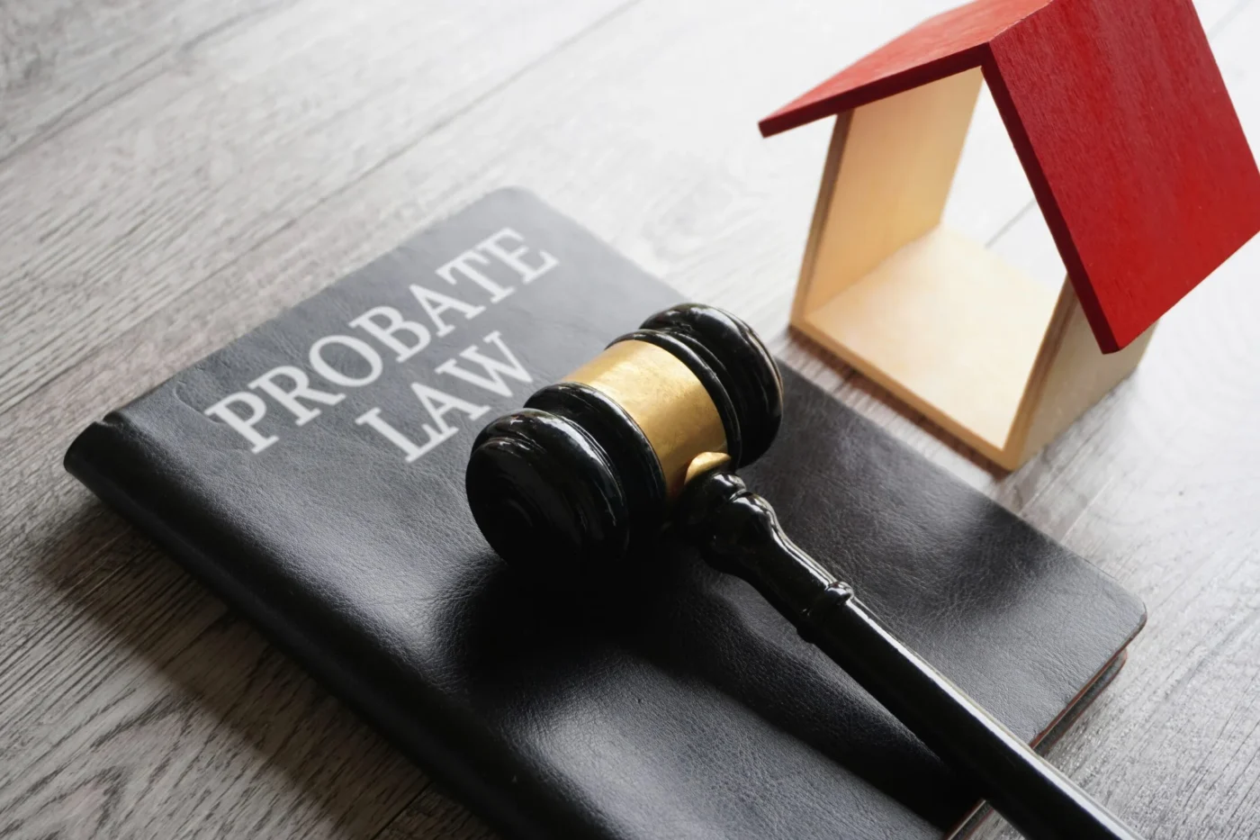 Gavel resting on a book titled “Probate Law” next to a small wooden model house on a gray wooden table.