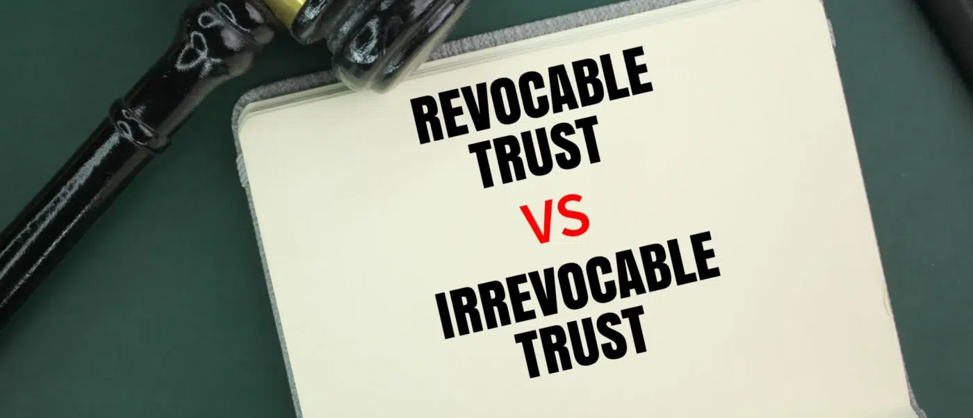 A notebook labeled “Revocable Trust vs Irrevocable Trust” beside a judge’s gavel and black pen on a green desk.