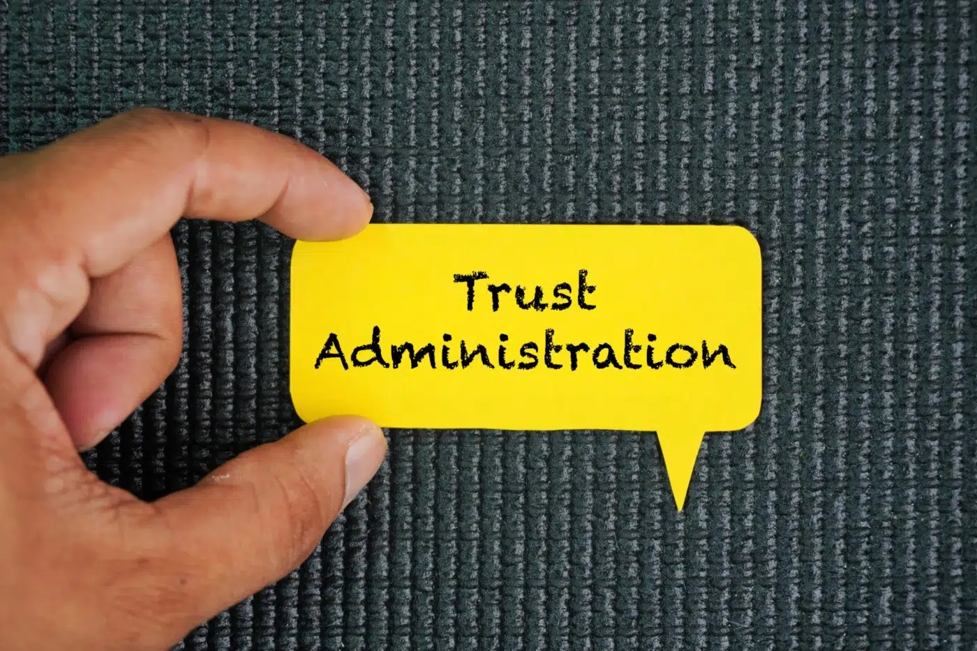 A hand holding a yellow speech-bubble card that displays the words “Trust Administration.”